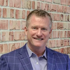 Dave St. Clair, in a blue check jacket against a brick wall.