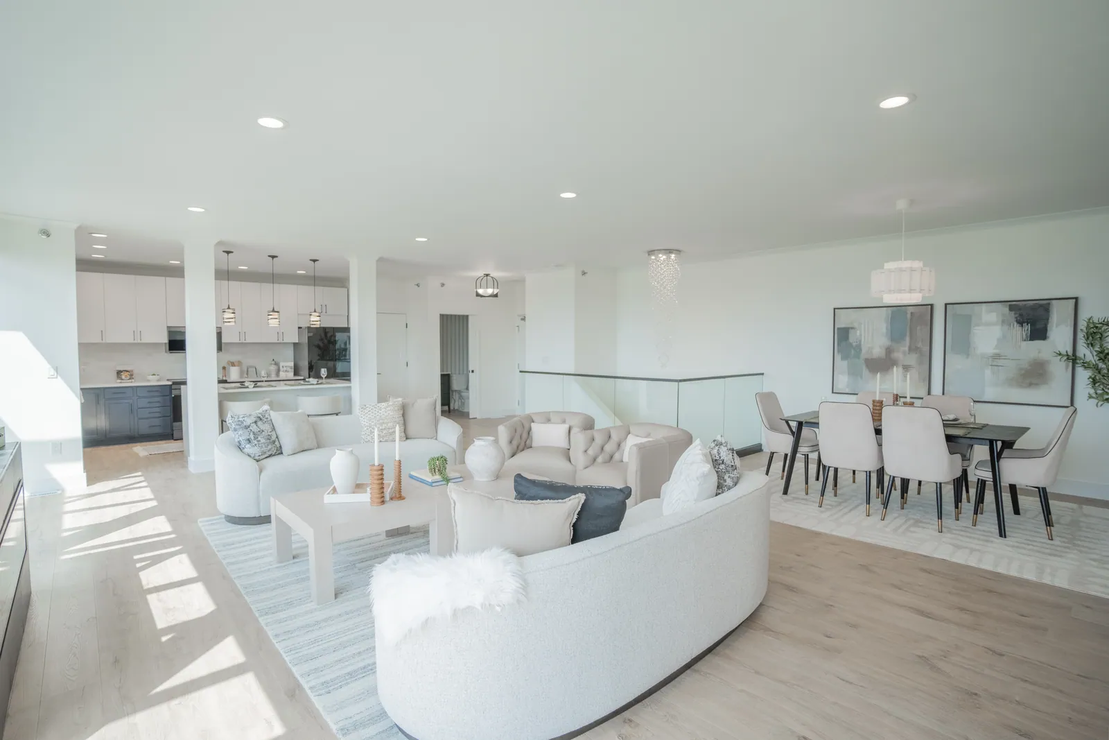 The great room of a two level River Rock residence seen from the seating area, with the dining table, glass rail, and kitchen beyond.