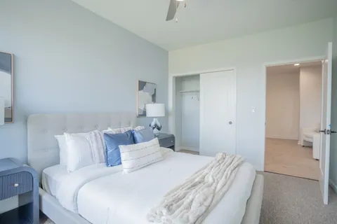 A bedroom in a single level River Rock residence with a gray upholstered bed and a closet.