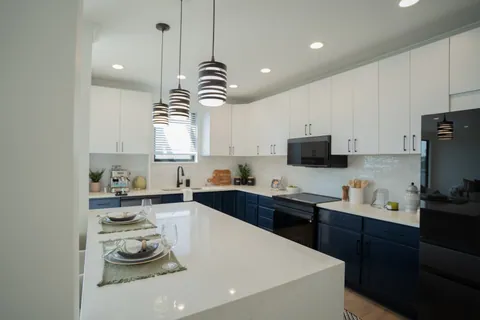 A River Rock kitchen from the island end, with the quartz waterfall island set for two, navy cabinetry, and three striped pendants.