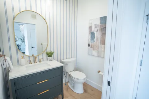 A River Rock powder room with striped wallpaper, a brass oval mirror, and a navy fluted vanity.