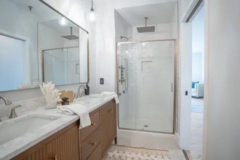 A River Rock primary bath with a fluted oak double vanity, marble counter, and a glass shower.