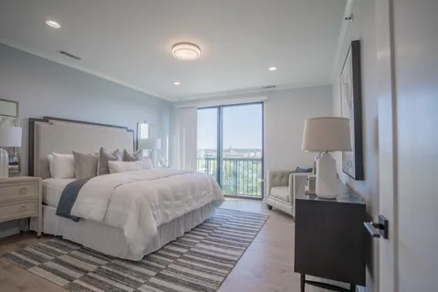 A River Rock primary bedroom with an upholstered bed and a sliding door open to the balcony and the view beyond.