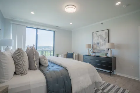 A River Rock primary bedroom from the bed, with the dresser, the armchair, and the window and balcony door open to the view.