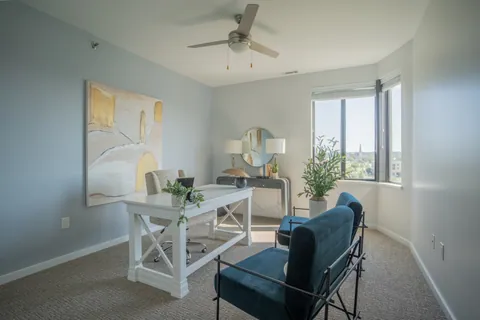 A study in a River Rock residence with a white desk, two navy chairs, and a window over the rooftops.